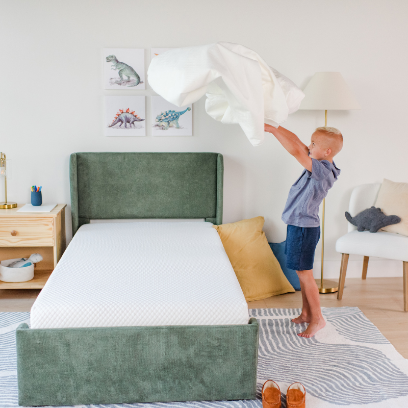 Child in green shirt and orange shorts lying on a textured white surface.