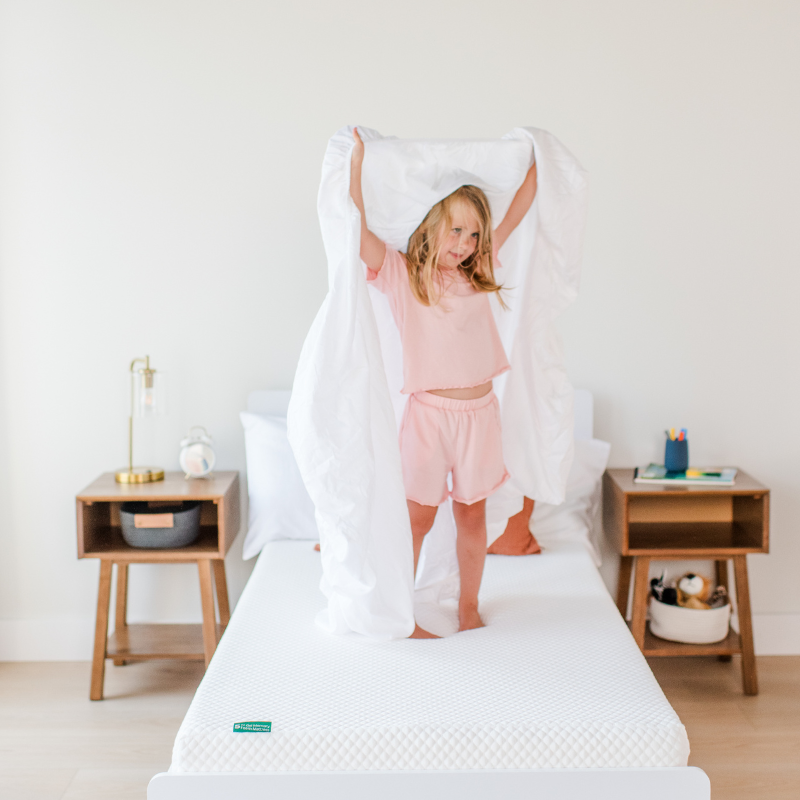 Child in green shirt and orange shorts lying on a textured white surface.