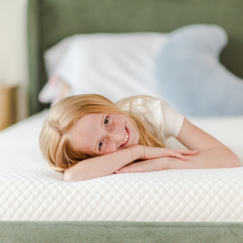 Child in green shirt and orange shorts lying on a textured white surface.