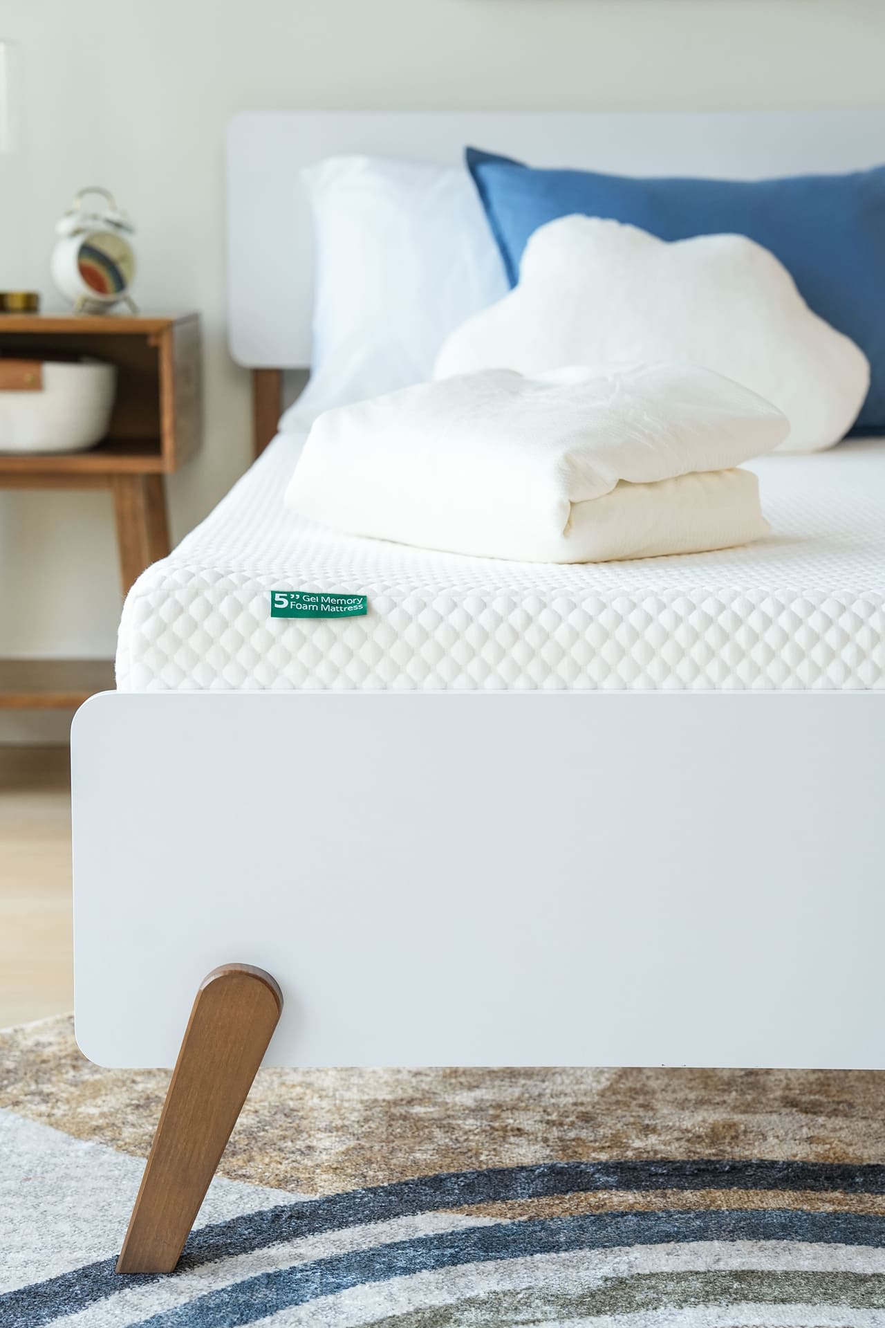 Memory foam mattress with white bedding and wooden bed frame in a modern bedroom.
