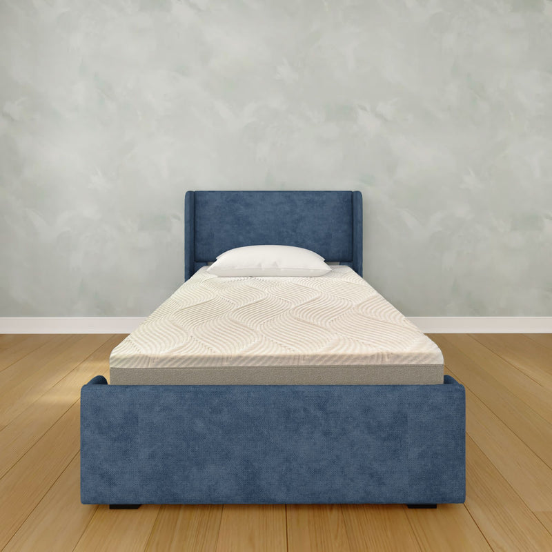 Blue upholstered single bed with white mattress and pillow on hardwood floor against a light textured wall