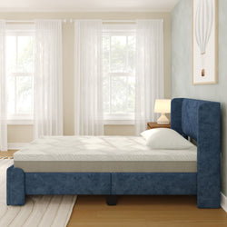 Blue upholstered platform bed with memory-foam mattress and white pillow in bright modern bedroom with sheer curtains, wooden nightstand, lamp and framed wall art