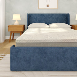 Blue upholstered bed frame with white mattress and pillows in modern bedroom featuring wooden nightstands and bedside lamps