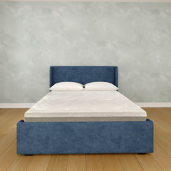 Modern blue upholstered platform bed with white pillows and textured mattress on hardwood floor in minimalist bedroom interior