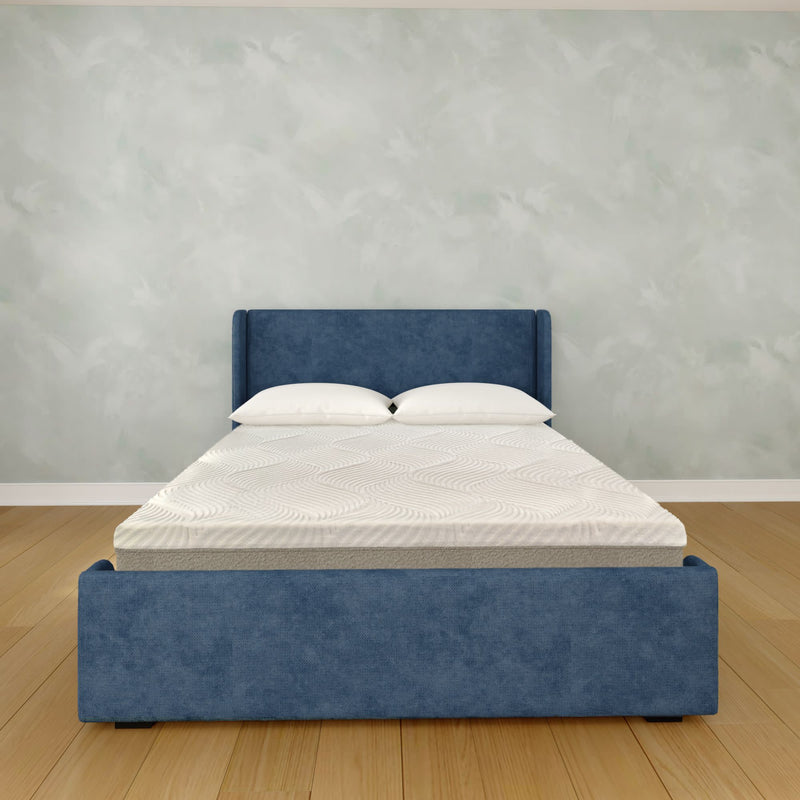 Modern blue upholstered platform bed with white pillows and textured mattress on hardwood floor in minimalist bedroom interior