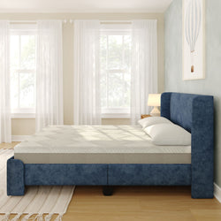 Modern navy blue upholstered platform bed with mattress and white pillows in a bright minimalist bedroom with sheer curtains, wooden floor and bedside lamp