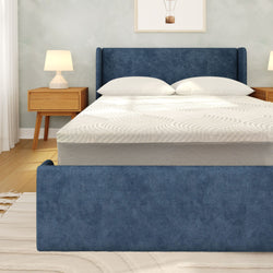 Modern bedroom interior with blue upholstered bed frame and footboard, white mattress and pillows, wooden nightstands with lamps on light hardwood floor