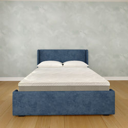 Modern blue upholstered bed frame with queen-size white mattress and pillows in a minimalist bedroom featuring a textured pale gray wall and hardwood floor