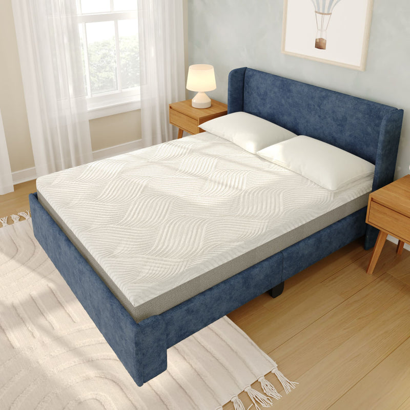 Queen-size blue upholstered bed with white textured mattress topper and pillows, wooden nightstands with lamp, hardwood floor and bright window in a modern bedroom