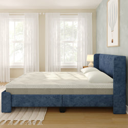 Navy blue upholstered platform bed with memory foam mattress and white pillows in a bright minimalist bedroom with sheer curtains, wooden floor, and bedside lamp