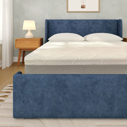 Blue upholstered bed frame with textured white mattress and pillows in modern bedroom with wooden nightstand and table lamp