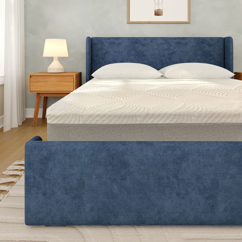 Blue upholstered bed frame with textured white mattress and pillows in modern bedroom with wooden nightstand and table lamp