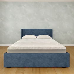 Modern blue upholstered platform bed with white mattress and pillows on hardwood floor against a light textured wall