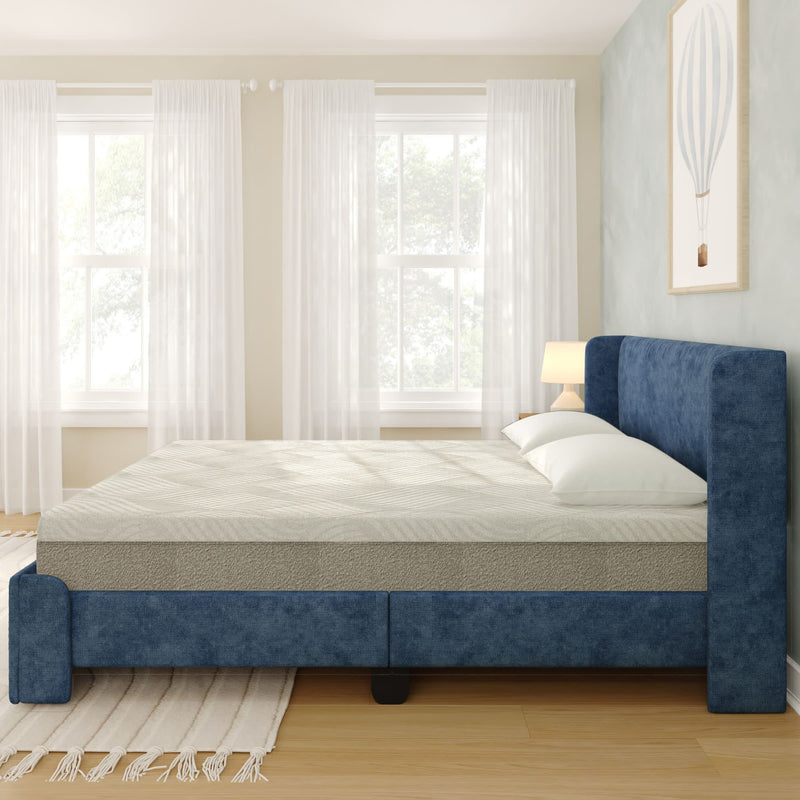 Modern navy upholstered bed with foam mattress and white pillows in bright minimalist bedroom with sheer curtains and hardwood floor