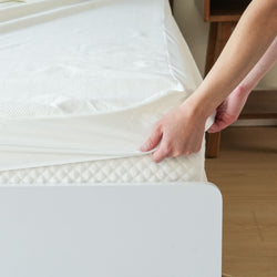 Hands adjusting a fitted sheet on a comfortable mattress for a neatly made bed.