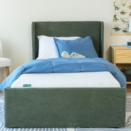 Green upholstered bed with blue bedding and plush toy, featuring a comfortable mattress in a cozy bedroom setting.