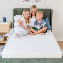 Mother and children reading a book on a comfortable mattress in a modern bedroom setting.